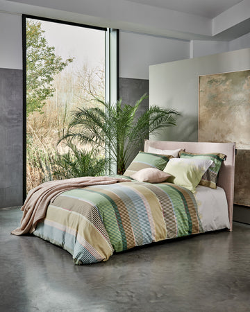 bed in een rustige setting met een groen dekbedovertrek met strepen in bruine en blauwe kleuren