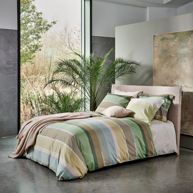 bed in een rustige setting met een groen dekbedovertrek met strepen in bruine en blauwe kleuren