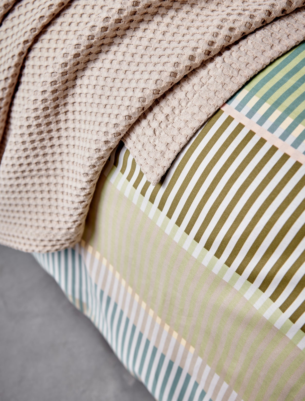 detail shot van een beige plaid en een dekbedovertrek met strepen in groene, blauwe en bruine kleuren