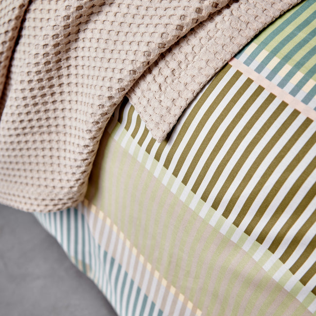 detail shot van een beige plaid en een dekbedovertrek met strepen in groene, blauwe en bruine kleuren