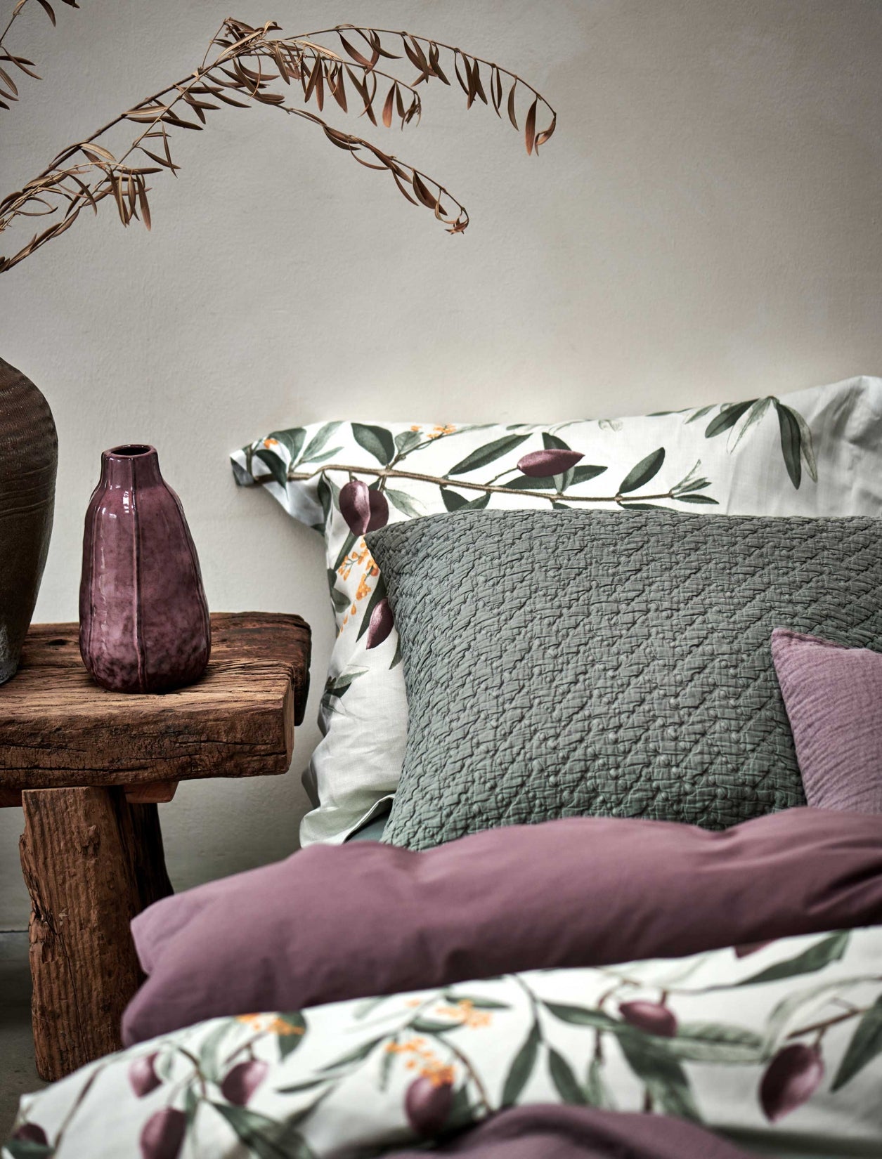 detail shot van een bed met een dekbedovertrek in een lichtgroene kleur met olijftakken, een overtrek in een paarse kleur en een sierkussen in een groene kleur