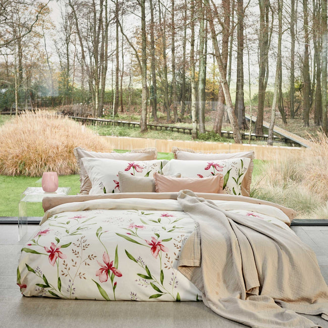 een bed in een rustige omgeving. Op het bed ligt een dekbedovertrek met roze bloemen en groene bladeren en een beige sprei