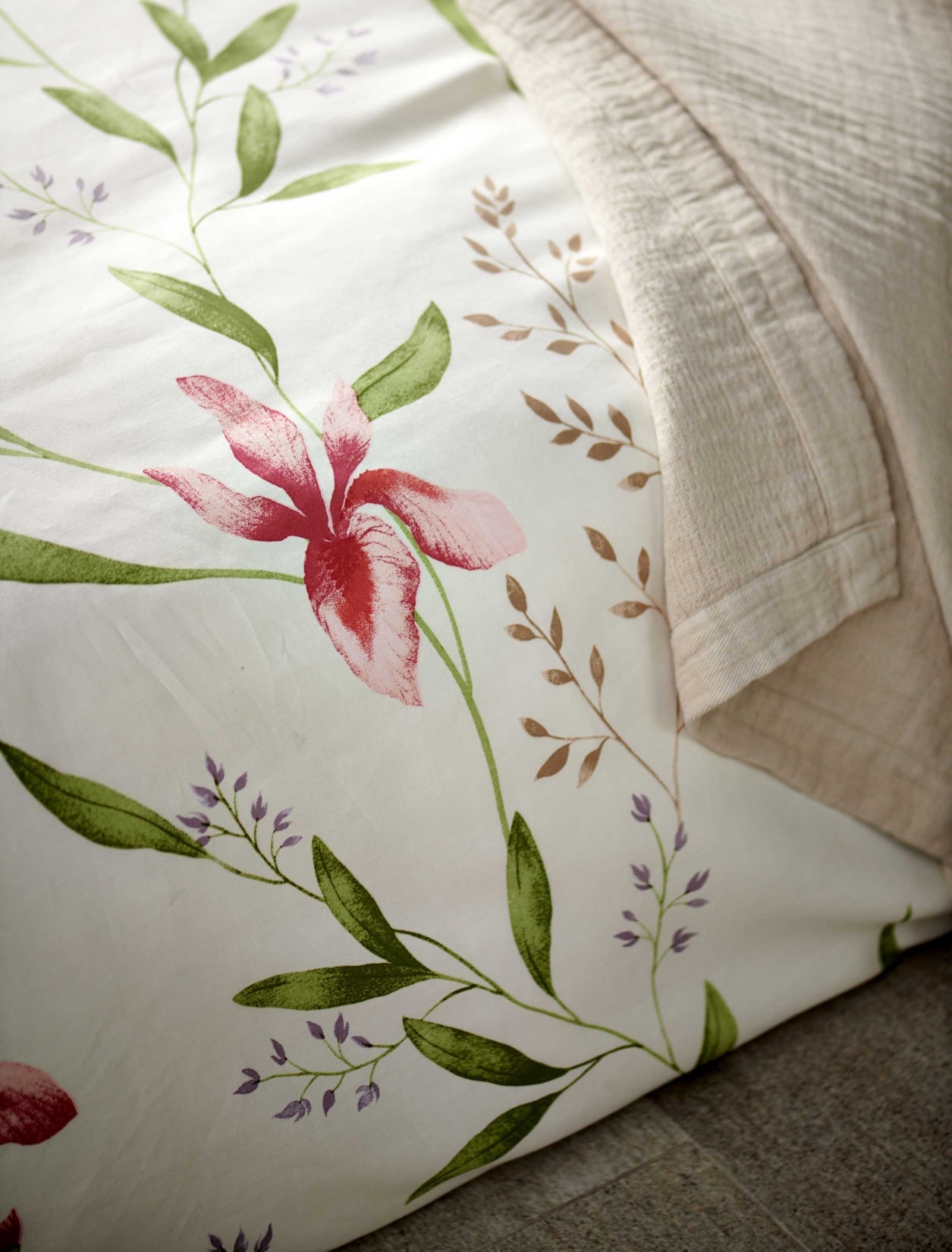 detail shot van een wit dekbedovertrek met roze bloemen en groene bladeren en een beige sprei