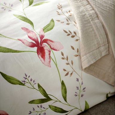 detail shot van een wit dekbedovertrek met roze bloemen en groene bladeren en een beige sprei
