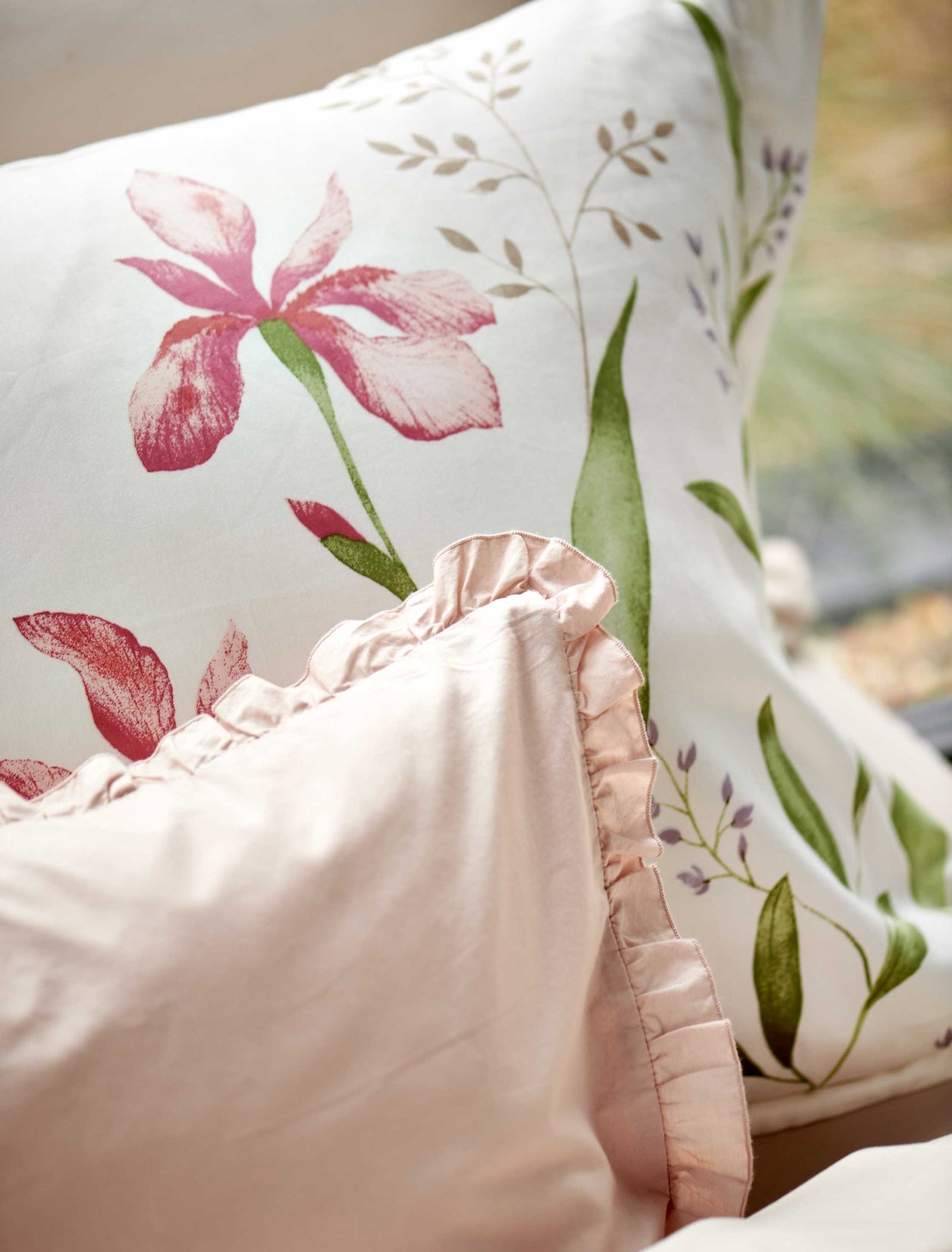 detail shot van een wit dekbedovertrek met roze bloemen en groene bladeren en een lichtroze sierkussen met ruffles