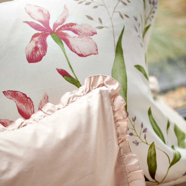 detail shot van een wit dekbedovertrek met roze bloemen en groene bladeren en een lichtroze sierkussen met ruffles