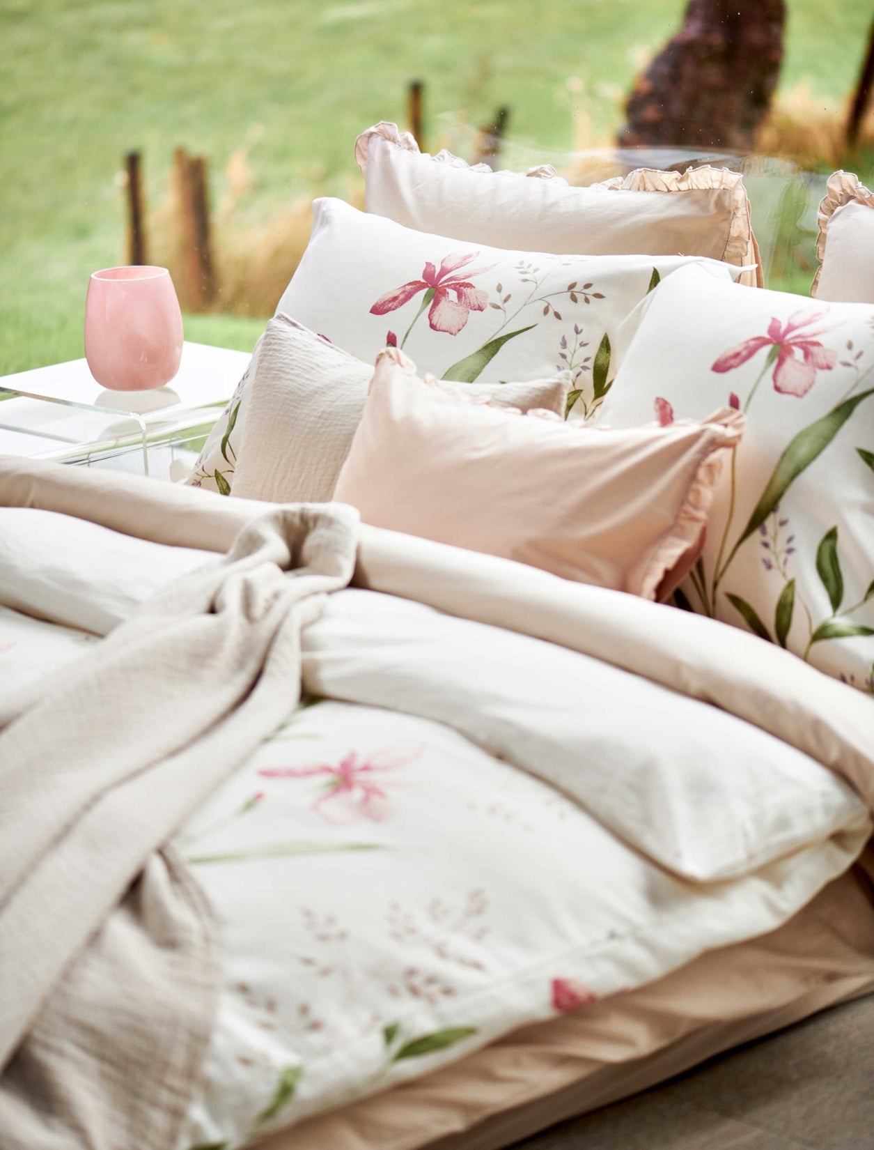 detail shot van een dekbedovertrek met roze bloemen en groene bladeren en een roze ruffle kussens. Op het bed ligt een beige sprei