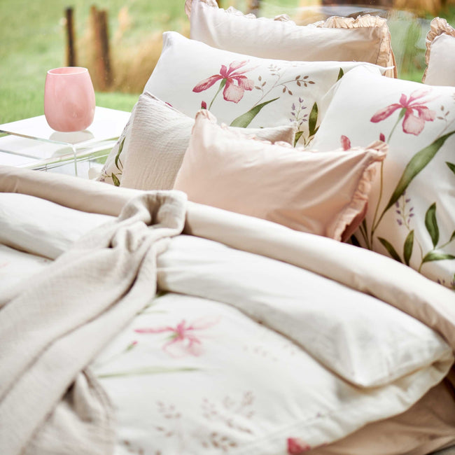 detail shot van een dekbedovertrek met roze bloemen en groene bladeren en een roze ruffle kussens. Op het bed ligt een beige sprei