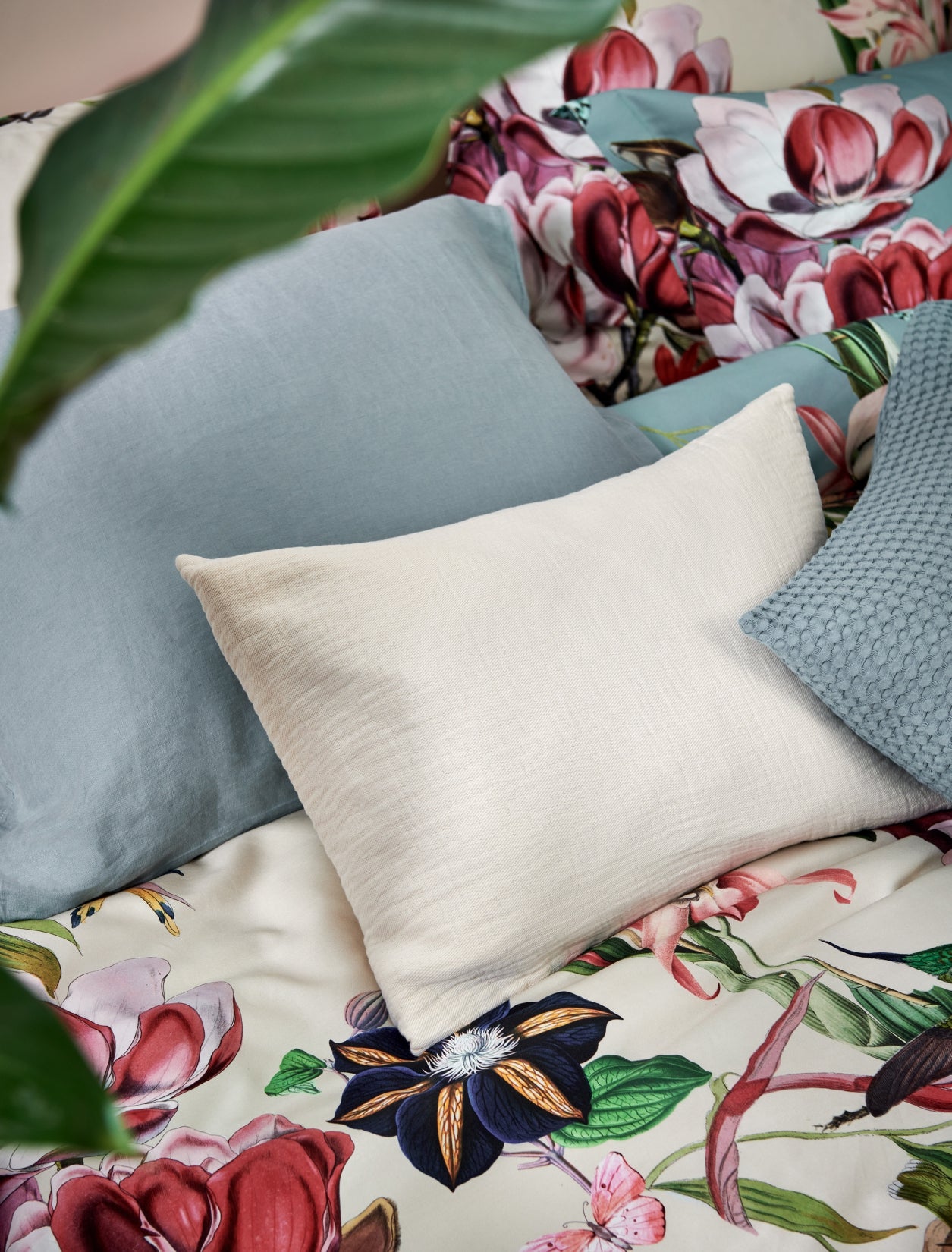 detail shot van een dekbedovertrek met bloemen en vogels en kussens in beige en blauwe kleuren