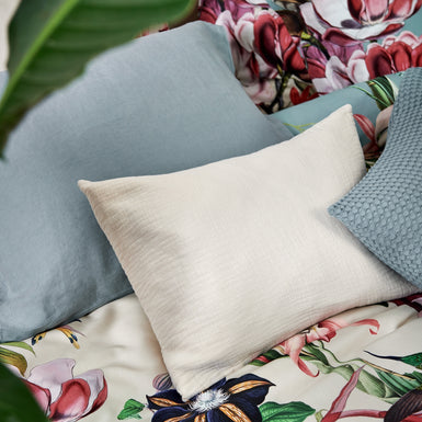 detail shot van een dekbedovertrek met bloemen en vogels en kussens in beige en blauwe kleuren