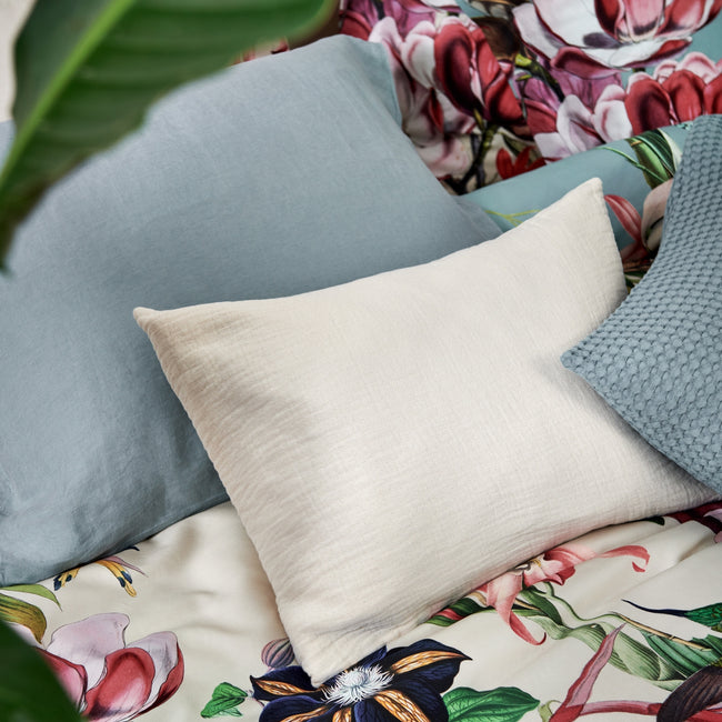 detail shot van een dekbedovertrek met bloemen en vogels en kussens in beige en blauwe kleuren