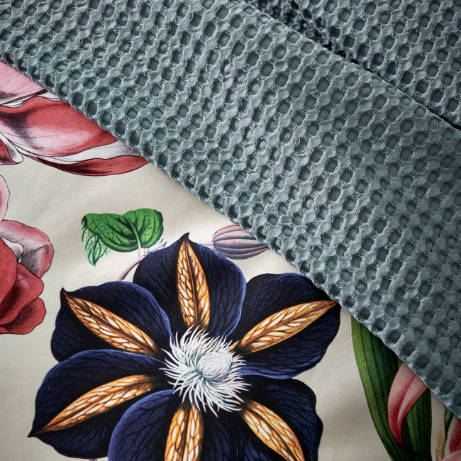 detail shot van een plaid met waffle structuur in een blauwe kleur en een dekbedovertrek met bloemen en een beige ondergrondkleur