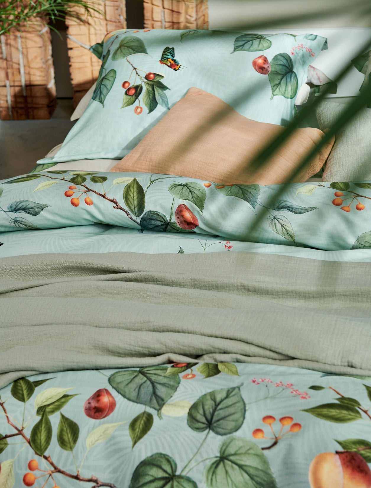 detail shot van een bed met een oranje kussen en een dekbedovertrek in lichtgroen met vruchten, bladeren en vlinders