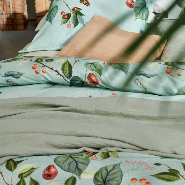 detail shot van een bed met een oranje kussen en een dekbedovertrek in lichtgroen met vruchten, bladeren en vlinders