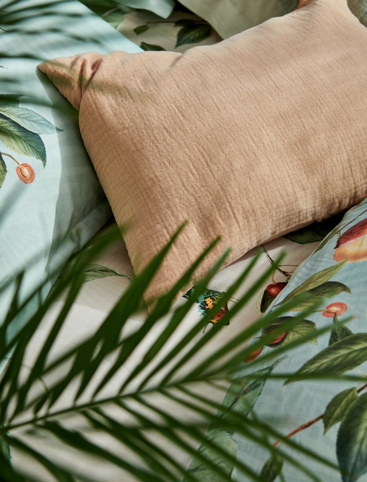 detail shot van een oranje kussen en een dekbedovertrek in lichtgroen en beige met vruchten, bladeren en vlinders