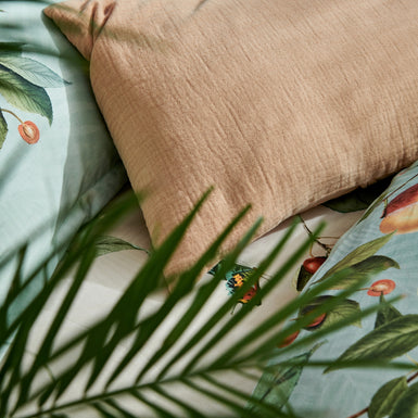 detail shot van een oranje kussen en een dekbedovertrek in lichtgroen en beige met vruchten, bladeren en vlinders