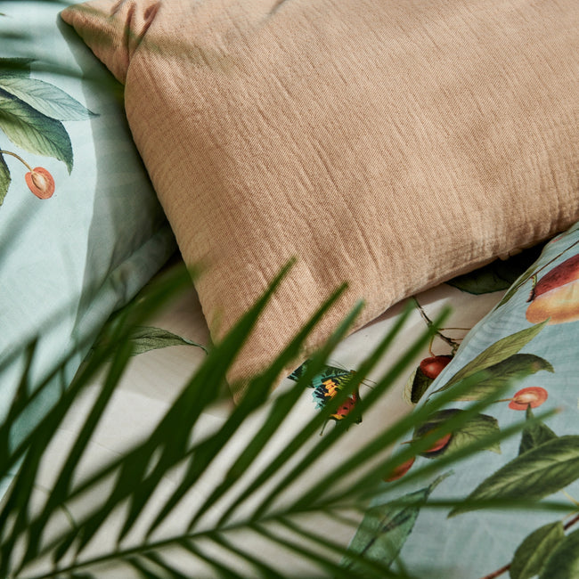 detail shot van een oranje kussen en een dekbedovertrek in lichtgroen en beige met vruchten, bladeren en vlinders