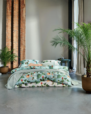 bed met een dekbedovertrek met vruchten, bladeren en vlinders in een groene en beige kleur in een rustige setting