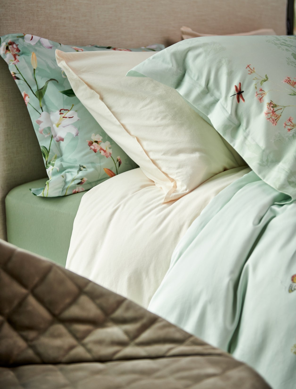 detail shot van een bed met een dekbedovertrek in een beige en groene kleur met bloemen