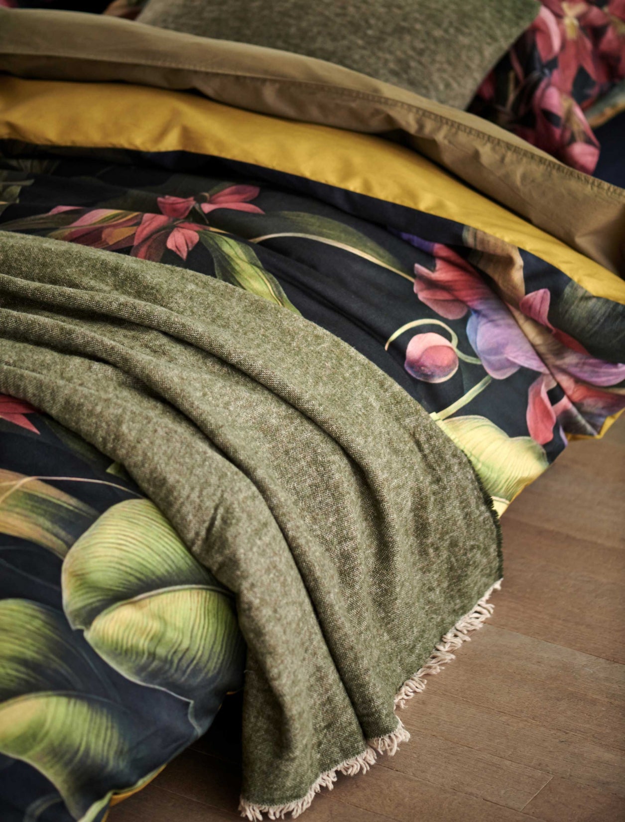detail shot van een bed met een overtrek met bloemen en planten en een wollen plaid in groen