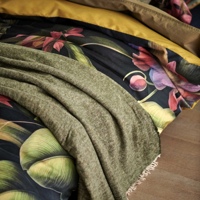 detail shot van een bed met een overtrek met bloemen en planten en een wollen plaid in groen