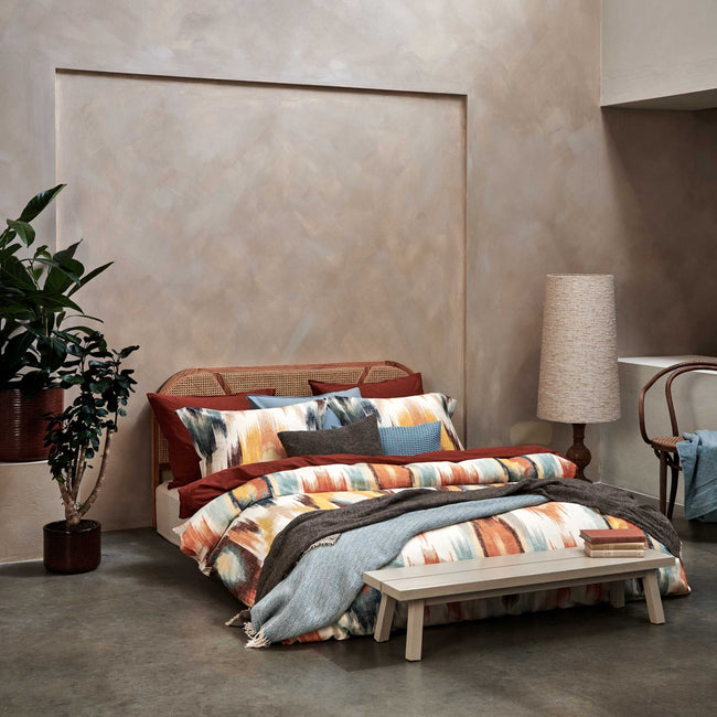 een bed in een rustige omgeving met een dekbedovertrek met print in oranje en blauwe kleuren 