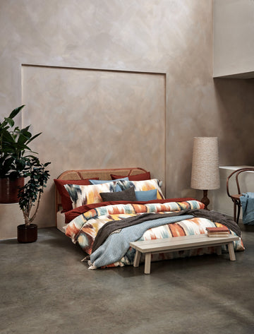 een bed in een rustige omgeving met een dekbedovertrek met print in oranje en blauwe kleuren 