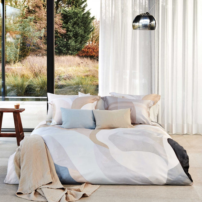 Een bed in een rustige omgeving met dekbedovertrekken in pastelachtige kleuren beige en blauwe kleuren