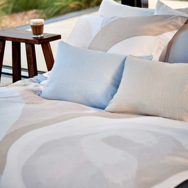 detail shot van een bed met een dekbedovertrek in zachte beige en blauwe kleuren en sierkussens in een beige en lichtblauwe kleur