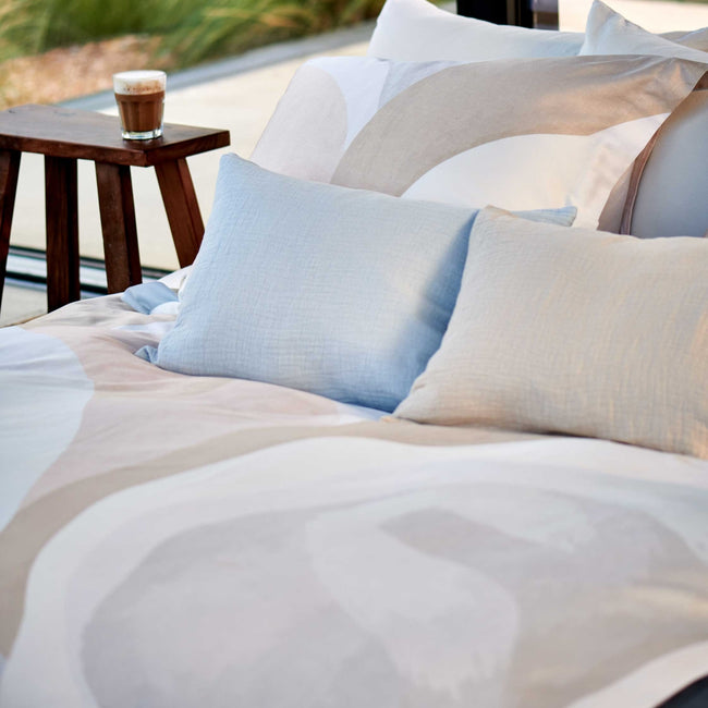detail shot van een bed met een dekbedovertrek in zachte beige en blauwe kleuren en sierkussens in een beige en lichtblauwe kleur