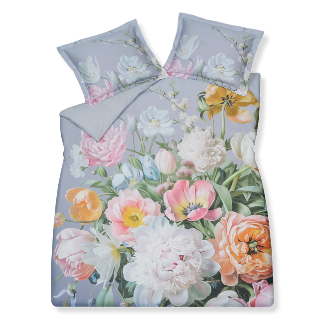 Fleur Festive lavender blue dekbedovertrek heeft hele grote bloemen in lichte pasteltinten in blauw, roze en oranje schakeringen op een blauw / paarse achtergrond. De achterkant van het dekbedovertrek is effen beige. De kussens hebben aan beide kanten een paar bloemen en een bloesemtak.