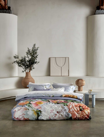 FLEUR FESTIVE dekbedovertrekset | lavender blue Fleur Festive lavender blue dekbedovertrek heeft hele grote bloemen in lichte pasteltinten in blauw, roze en oranje schakeringen op een blauw / paarse achtergrond. De achterkant van het dekbedovertrek is effen beige. De kussens hebben aan beide kanten een paar bloemen en een bloesemtak.