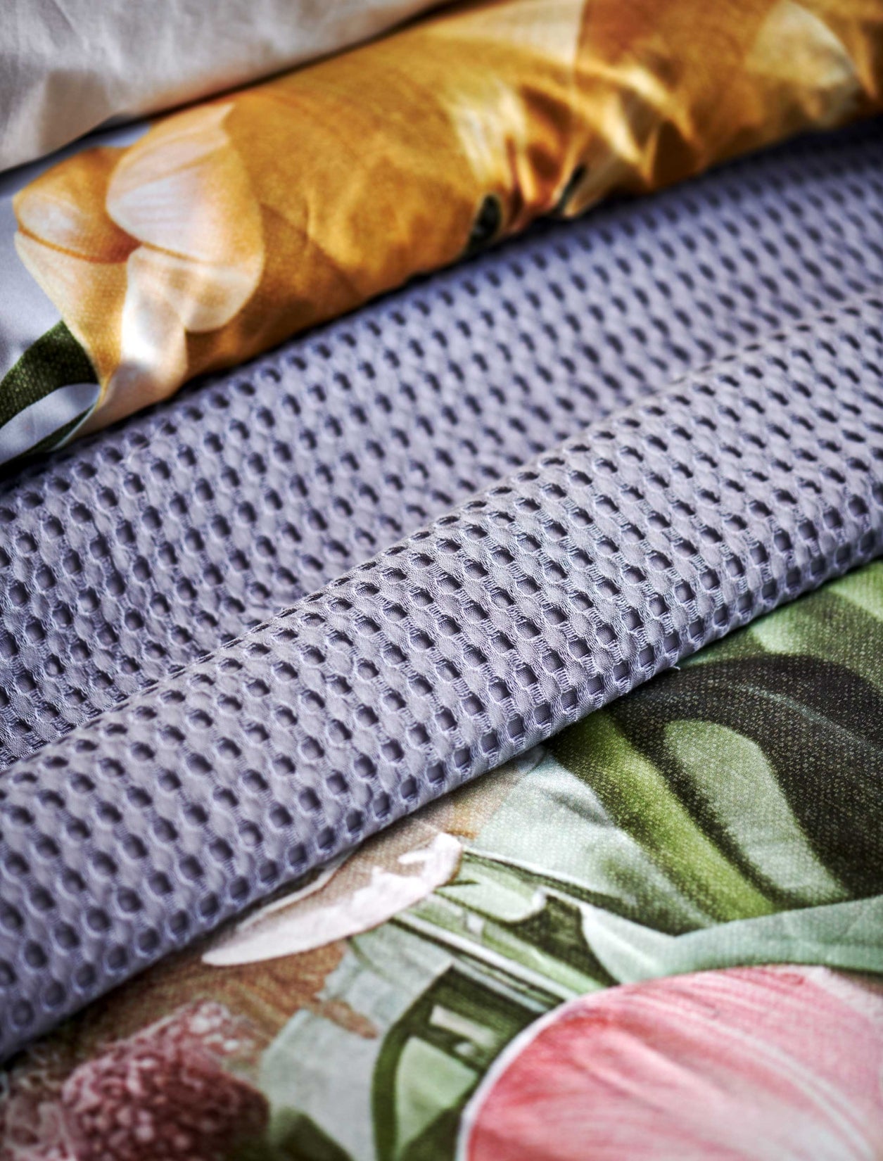 Fleur Festive lavender blue dekbedovertrek heeft hele grote bloemen in lichte pasteltinten in blauw, roze en oranje schakeringen op een blauw / paarse achtergrond. De achterkant van het dekbedovertrek is effen beige. De kussens hebben aan beide kanten een paar bloemen en een bloesemtak.
