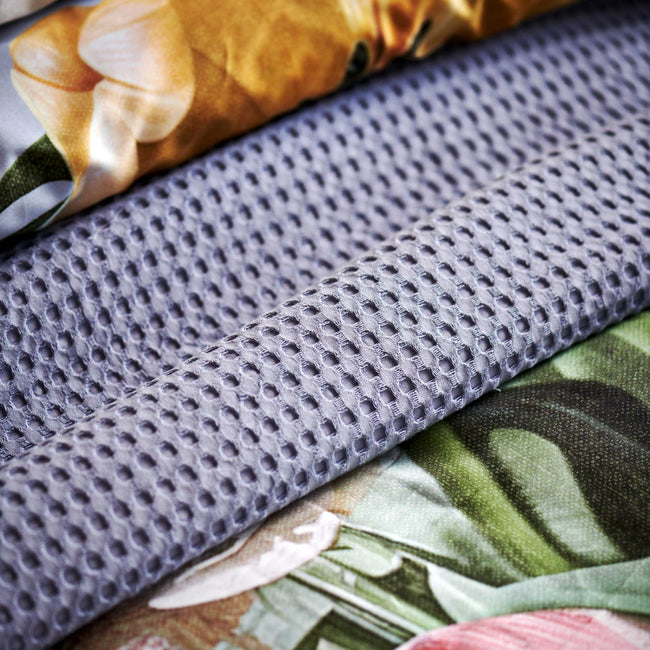 Fleur Festive lavender blue dekbedovertrek heeft hele grote bloemen in lichte pasteltinten in blauw, roze en oranje schakeringen op een blauw / paarse achtergrond. De achterkant van het dekbedovertrek is effen beige. De kussens hebben aan beide kanten een paar bloemen en een bloesemtak.