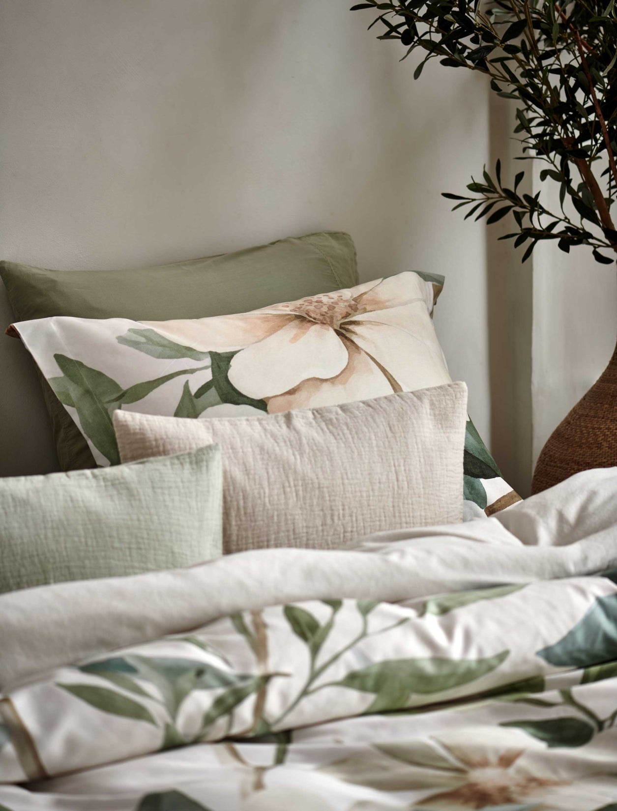 detail shot van een hoofdkussen met gele en groene bloemen en sierkussens in groene en beige kleuren.