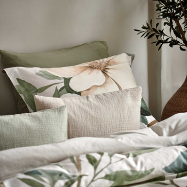 detail shot van een hoofdkussen met gele en groene bloemen en sierkussens in groene en beige kleuren.