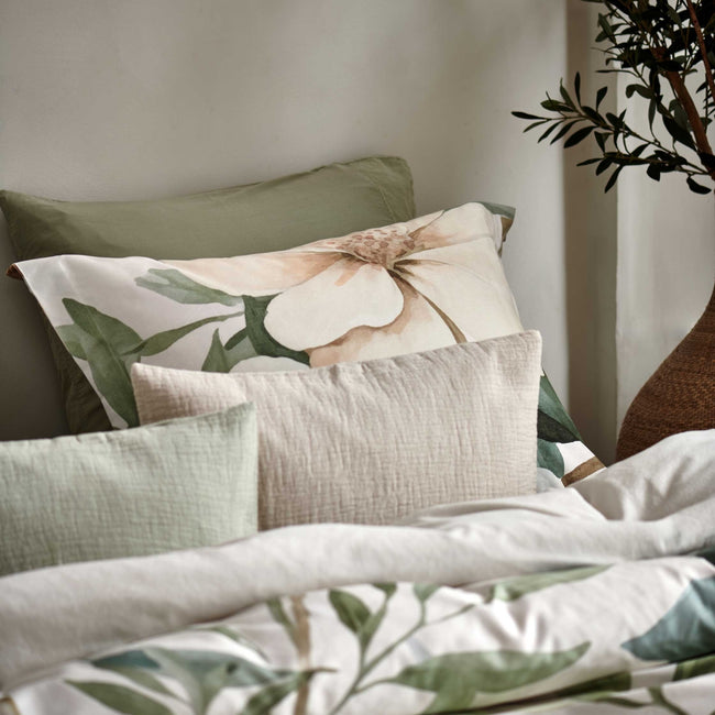detail shot van een hoofdkussen met gele en groene bloemen en sierkussens in groene en beige kleuren.