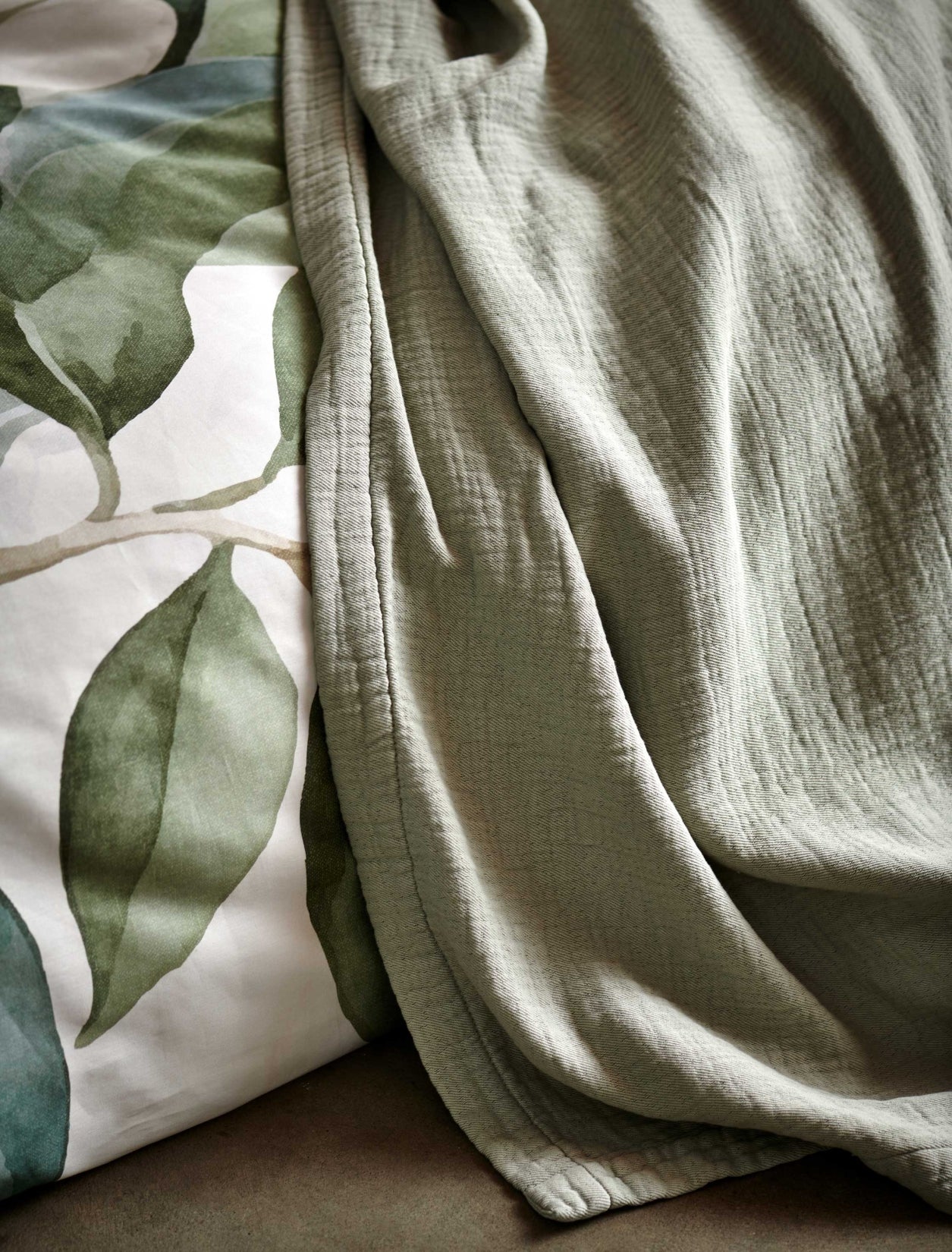 detail shot van een plaid in een zacht groene kleur en een dekbedovertrek met groene bladeren