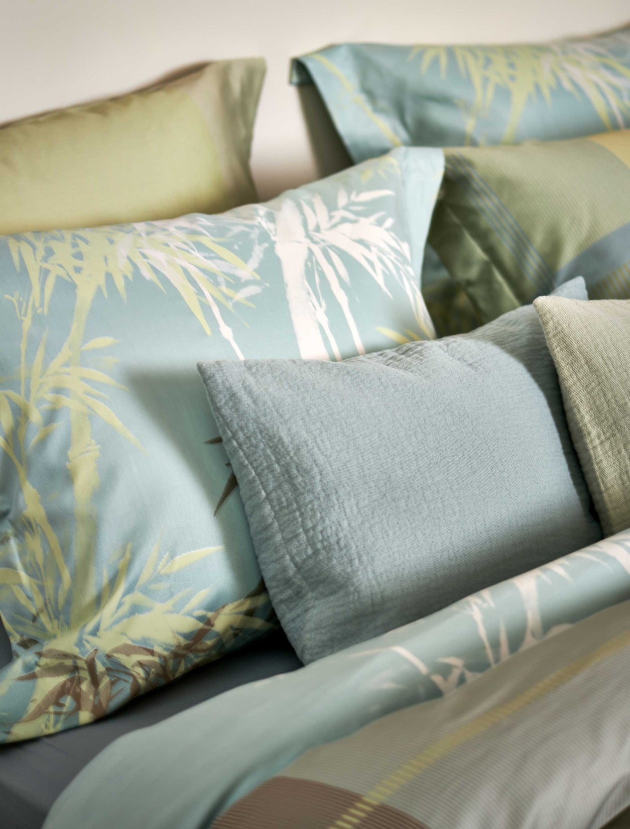 detail shot van een hoofdkussen met palmbomen in groene en blauwe kleuren en een sierkussen in een licht blauwe kleur