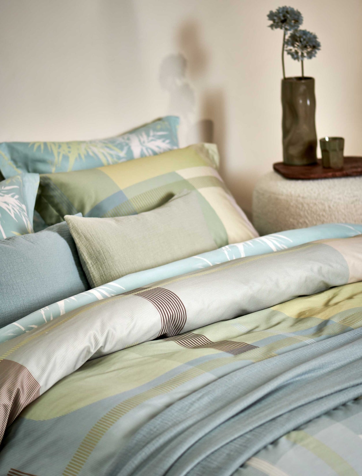 detail shot van een bed met een dekbedovertrek met groene en blauwe kleuren in een grafische print en een plaid in een blauwe kleur