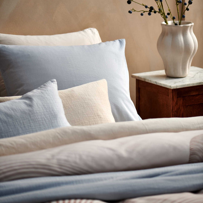 detail shot van een bed met daarop een dekbedovertrek in beige en blauwe kleuren en een hoofdkussen in beige en lichtblauwe kleuren