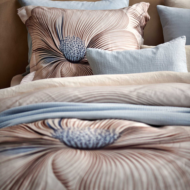 detail shot van een bed met een beige dekbedovertrek met een grote bloem als print in bruine en lichtblauwe kleuren