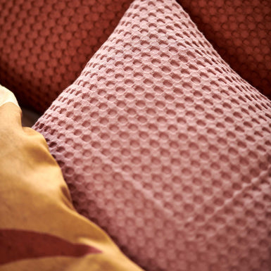 Sunset Nights multi dekbedovertrek heeft verschillende soorten bladeren in een abstracte tekenstijl in bruin, roze en rood. De achterkant van het dekbedovertrek is effen beige. De kussens hebben een kleinere versie van de bladeren.
