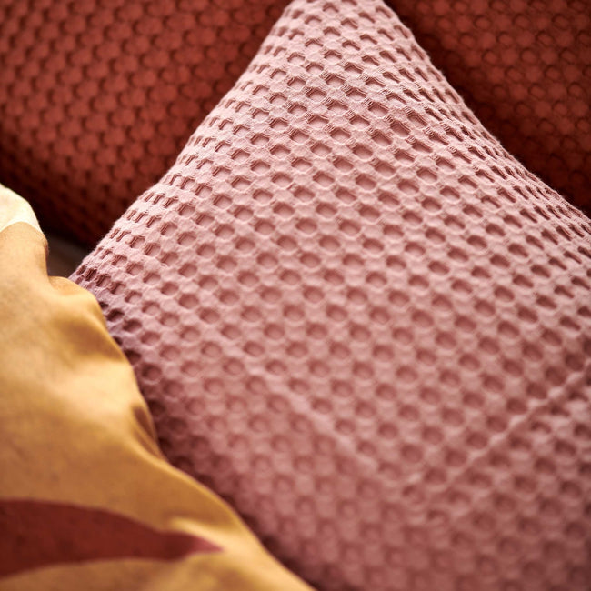 Sunset Nights multi dekbedovertrek heeft verschillende soorten bladeren in een abstracte tekenstijl in bruin, roze en rood. De achterkant van het dekbedovertrek is effen beige. De kussens hebben een kleinere versie van de bladeren.