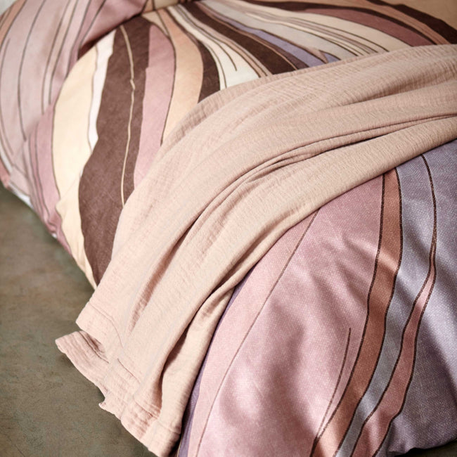 Swirls moonscape dekbedovertrek heeft een abstracte versie van een marmerpatroon met paars, roze en bruine tinten. De achterkant van het dekbedovertrek is effen offwhite. De kussens hebben aan beide zijden hetzelfde patroon. 