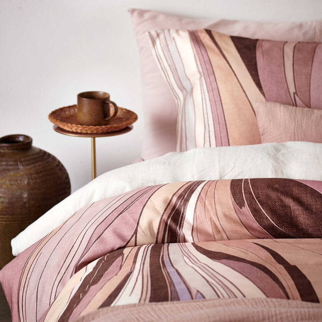 Swirls moonscape dekbedovertrek heeft een abstracte versie van een marmerpatroon met paars, roze en bruine tinten. De achterkant van het dekbedovertrek is effen offwhite. De kussens hebben aan beide zijden hetzelfde patroon. 