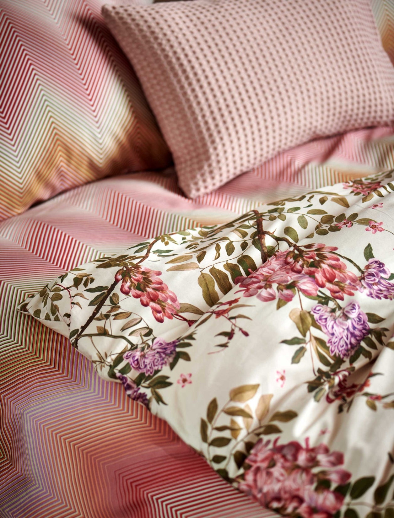 detail shot van een dekbedovertrek met roze en paarse bloemen en een dekbedovertrek met zigzag print in roze en oranje kleuren