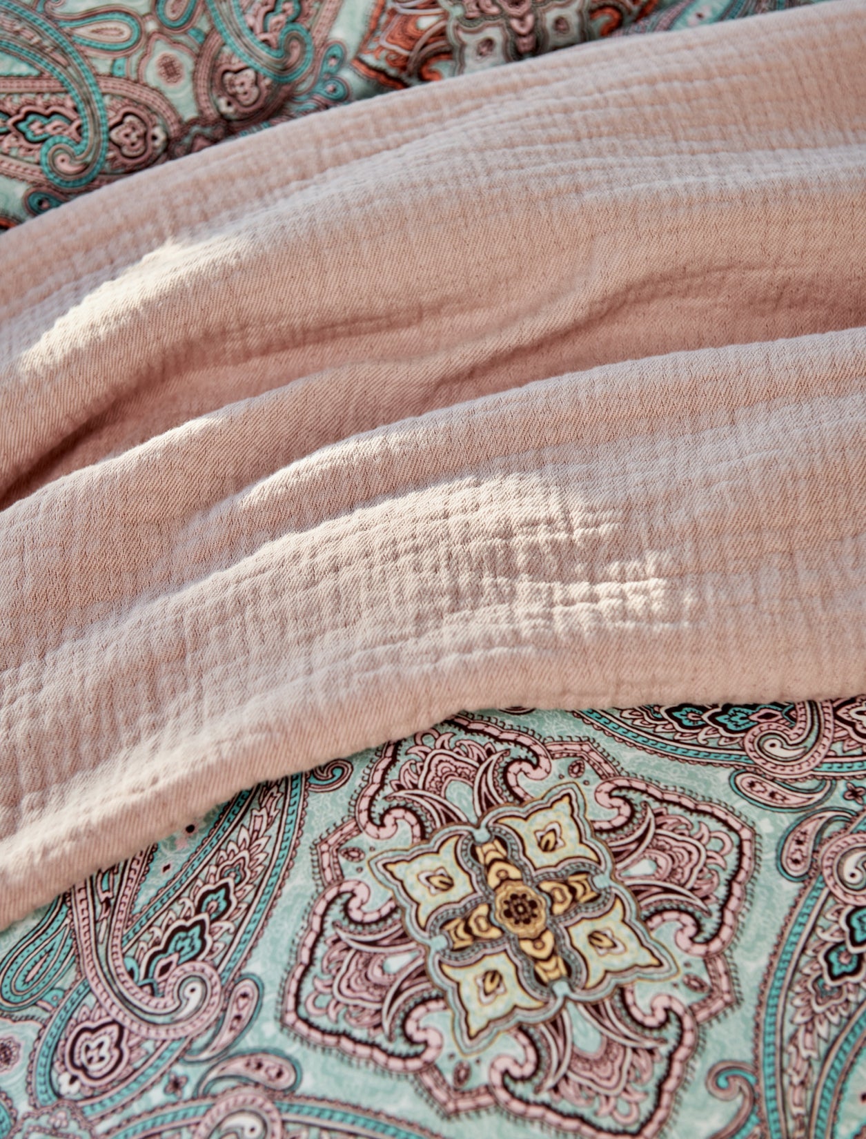 detail shot van een plaid in roze kleur en een dekbedovertrek met paisley print in blauw en roze