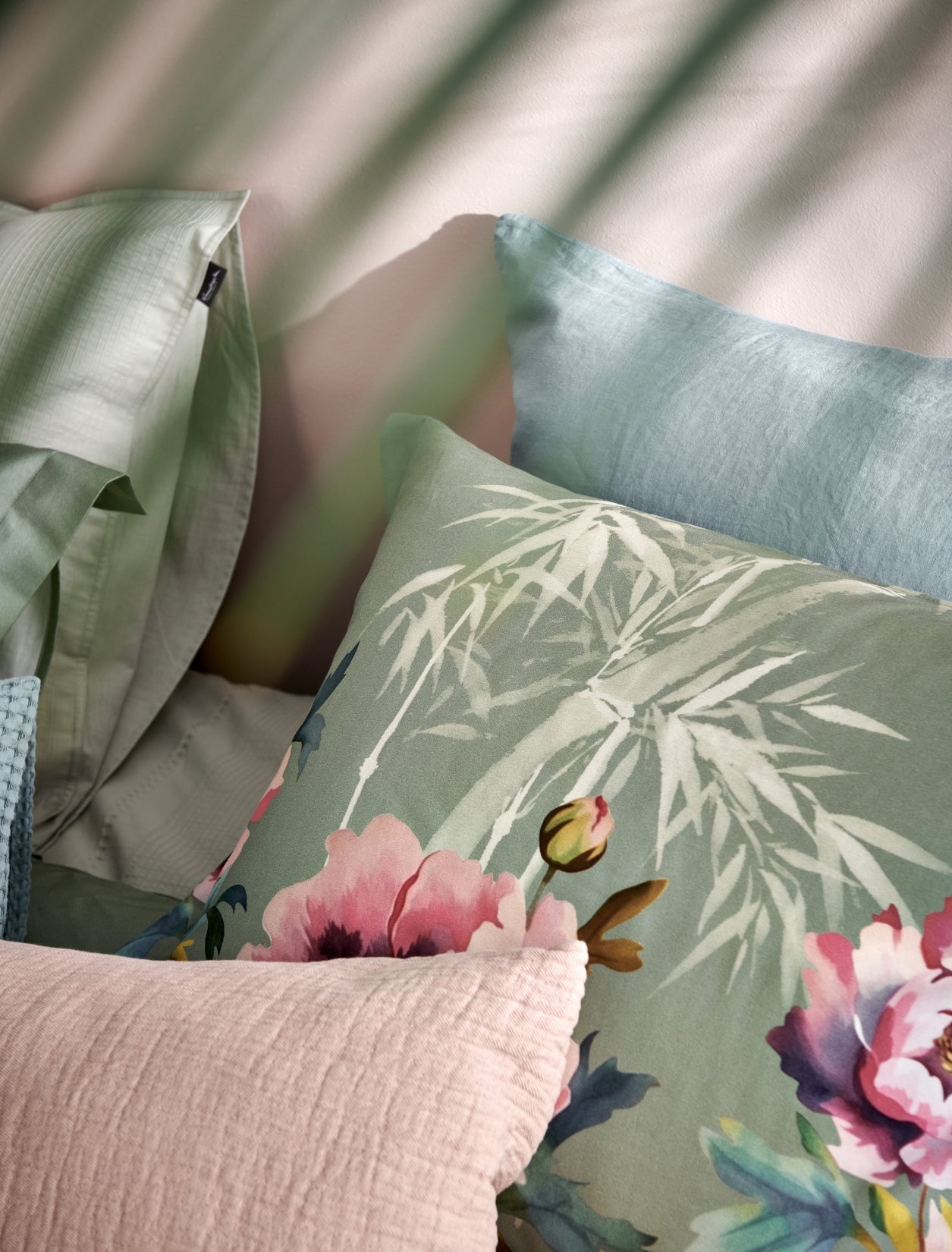 detail shot van een hoofdkussen in een groene kleur met roze bloemen en bamboe takken