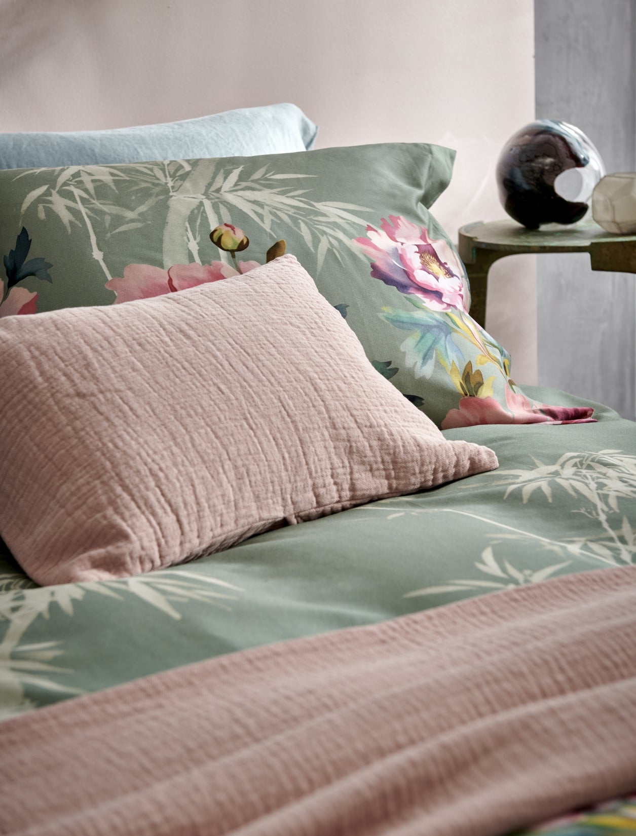 detail shot van een bed met een dekbedovertrek in een groene kleur met roze bloemen en bamboe takken en een roze kussen